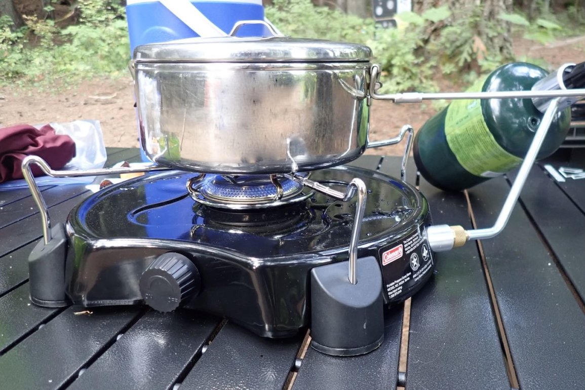 This photo shows the Coleman PowerPack Propane Stove for camping being used to cook on a camping table.