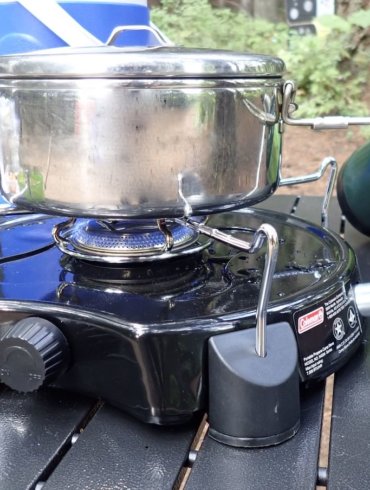 This photo shows the Coleman PowerPack Propane Stove for camping being used to cook on a camping table.