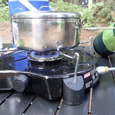 This photo shows the Coleman PowerPack Propane Stove for camping being used to cook on a camping table.