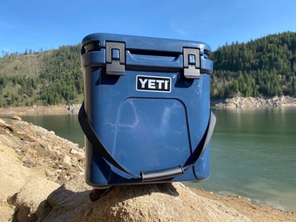 This photo shows the YETI Roadie 24 hard cooler outside near a lake on a day trip.