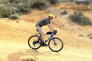 This testing and review photo shows the author wearing the Showers Pass Gravel 10" Shorts while riding a gravel bike on a trail during testing.
