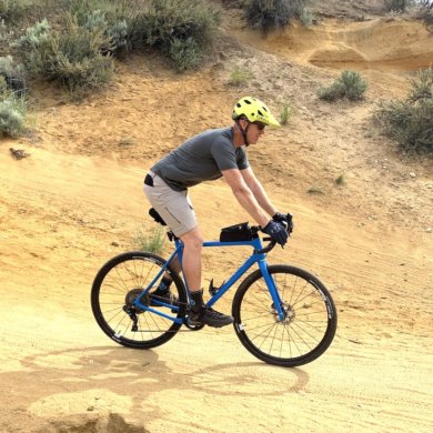 This testing and review photo shows the author wearing the Showers Pass Gravel 10" Shorts while riding a gravel bike on a trail during testing.