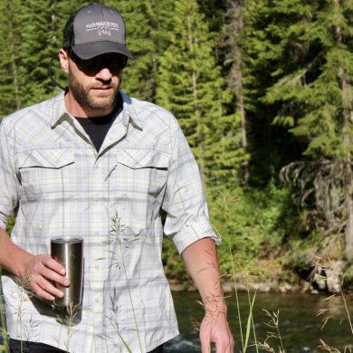 This photo shows the author wearing, testing, and reviewing the Stio Eddy Drift LS shirt near a river.