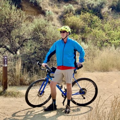 This review and testing photo shows the author wearing the Showers Pass Ultralight Wind Jacket on a trail with a gravel bike.
