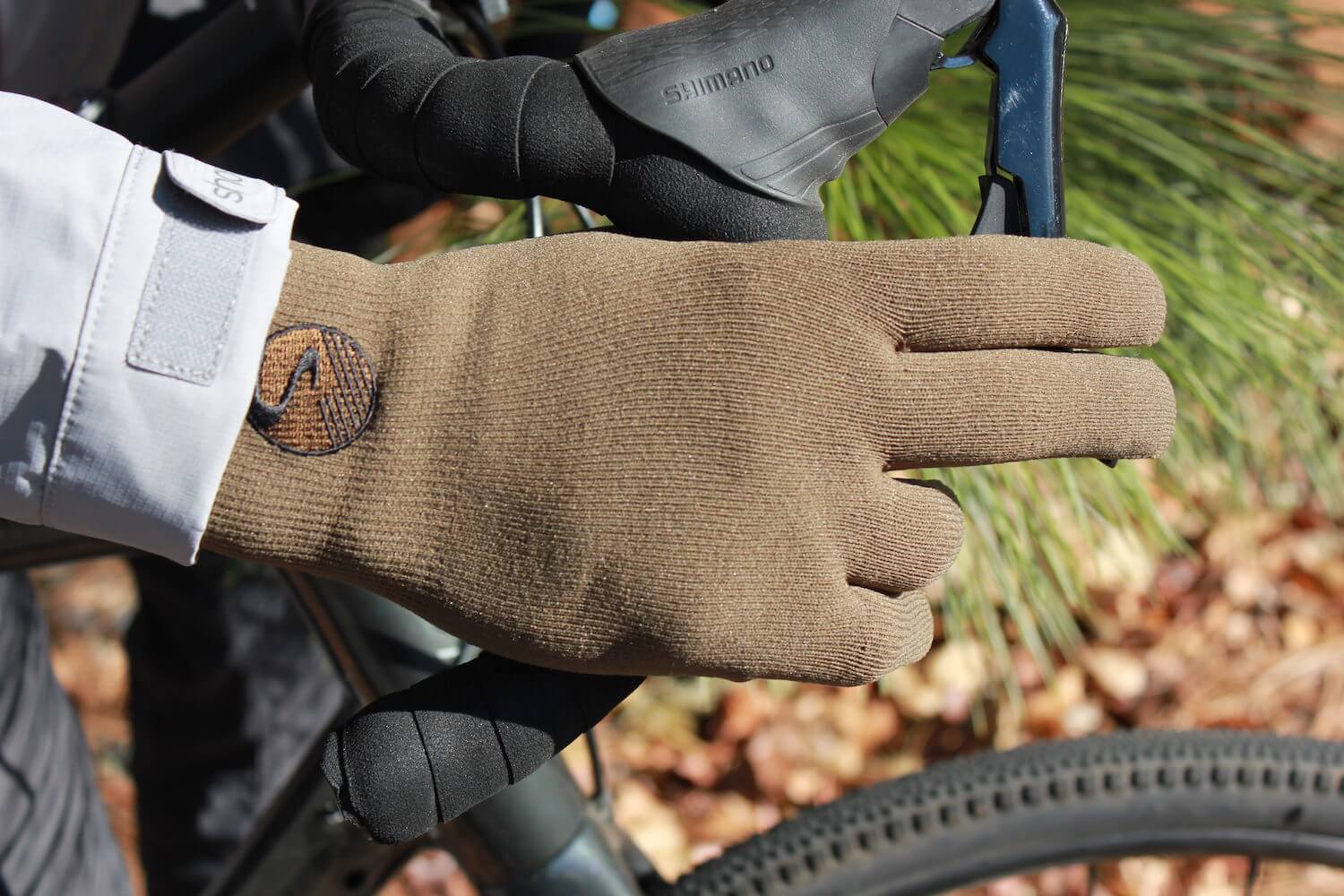 This review photo shows the Showers Pass Crosspoint Waterproof Knit Wool Gloves being worn on a gravel bike by the author.