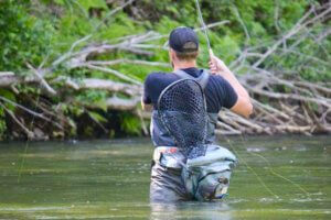 This photo shows the author storing a mid-length fishing net in a lumbar fly fishing pack while fishing in a river.