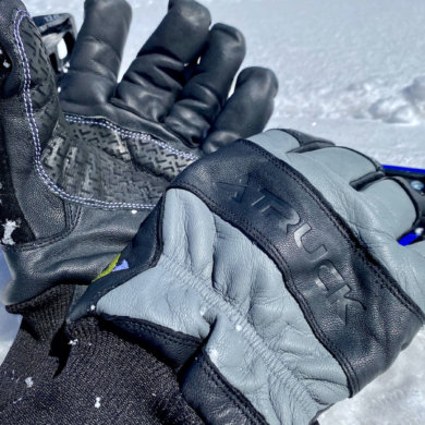 This review photo shows the TRUCK M1 Pro ski and snowboard gloves next to skis in the snow durning the testing process.