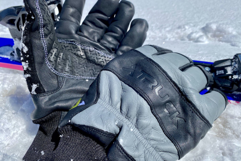 This review photo shows the TRUCK M1 Pro ski and snowboard gloves next to skis in the snow durning the testing process.