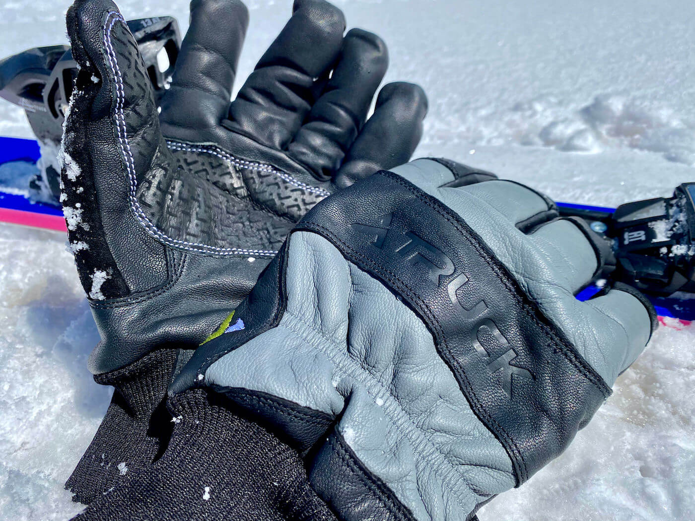 This review photo shows the TRUCK M1 Pro ski and snowboard gloves next to skis in the snow durning the testing process.