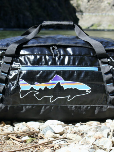 This review photo shows the Patagonia Black Hole Duffel Bag 55L version outside near a river during the testing process.