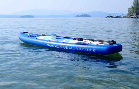 This photo shows the Outdoor Master Chasing Blue 'Infinite' iSUP inflated and floating on a lake with its included paddle.