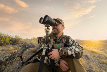 This photo shows a hunter using the Maven C.4 15x56 binoculars outside with a tripod.