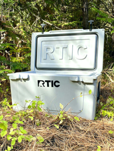 This testing and review photo shows the RTIC 65 QT Hard Cooler outside in a forest at a camping site.