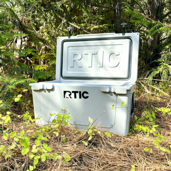 This testing and review photo shows the RTIC 65 QT Hard Cooler outside in a forest at a camping site.