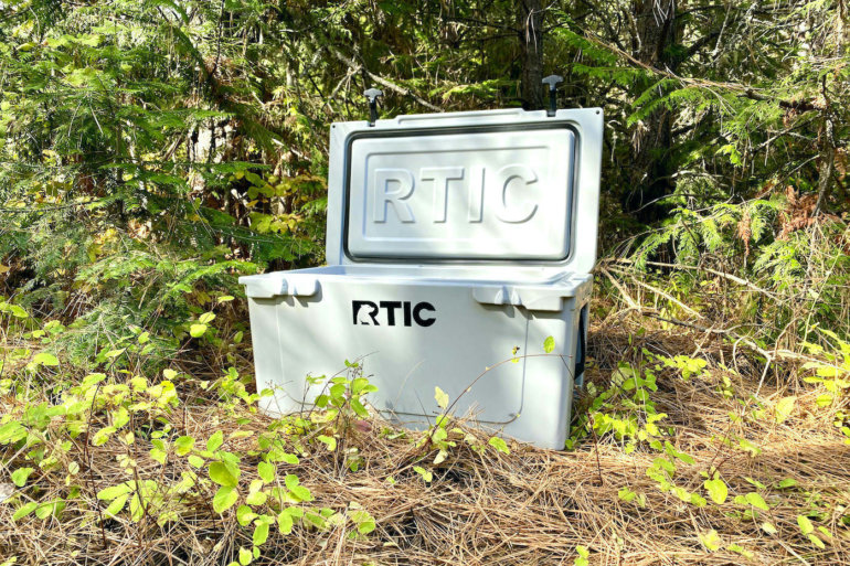 This testing and review photo shows the RTIC 65 QT Hard Cooler outside in a forest at a camping site.