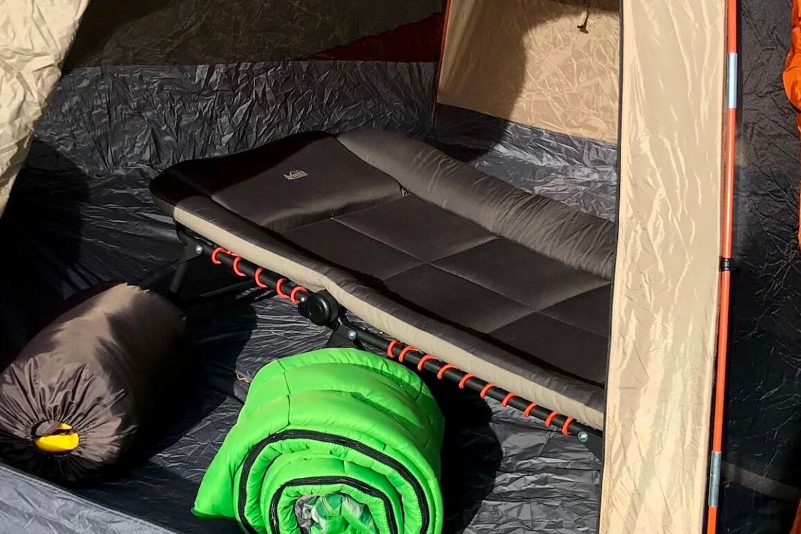 The best camping cot feature photo shows a cot setup inside a tent with sleeping bags.