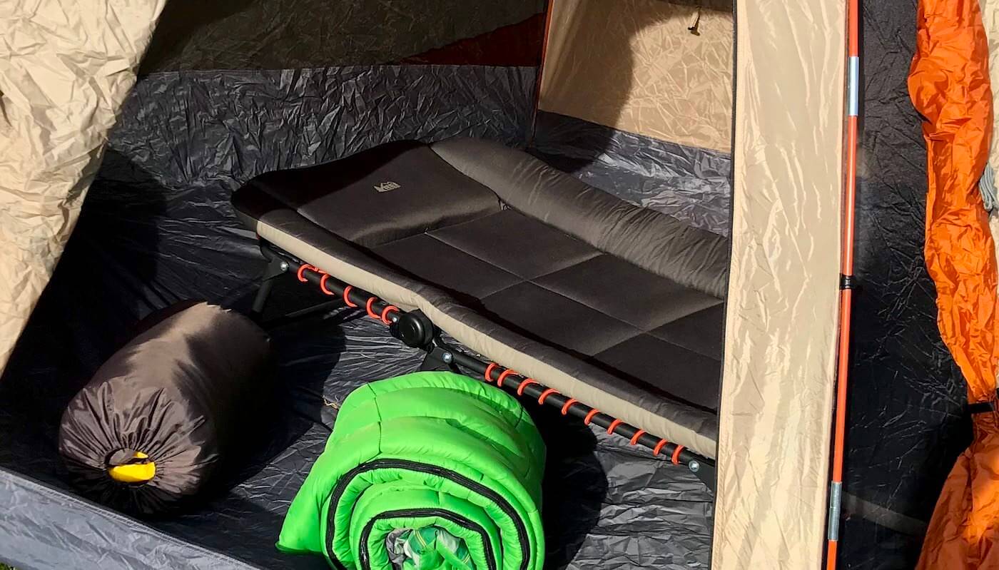 The best camping cot feature photo shows a cot setup inside a tent with sleeping bags.