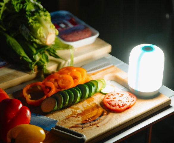 This photo shows the BioLite AlpenGlow 500 lit up in the dark next to a cutting board with vegetables.