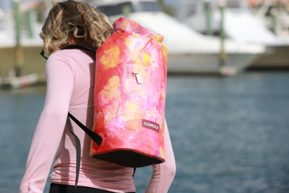 This photo shows a woman carrying the ICEMULE Jaunt backpack cooler outside near water.