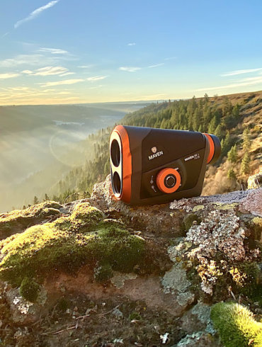This review photo shows the Maven RF.1 Rangefinder outside on a rock in a forested landscape.