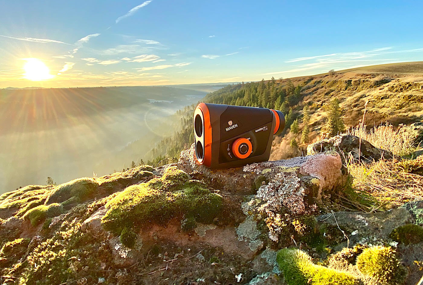 This review photo shows the Maven RF.1 Rangefinder outside on a rock in a forested landscape.