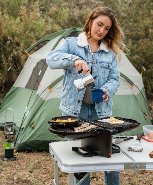 This photo shows an outdoorsy woman grilling on the nomadiQ Grill.