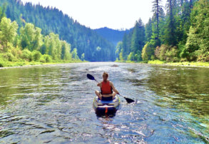 This photo shows an outdoorsy woman paddle boarding on a river.
