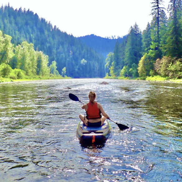This photo shows an outdoorsy woman paddle boarding on a river.
