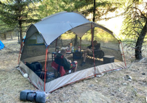 This photo shows outdoor enthusiasts inside of a screen house shelter while camping.