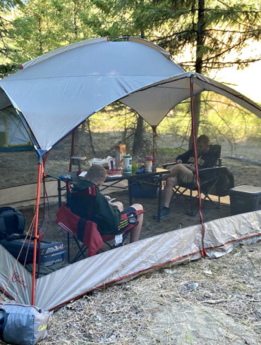 This photo shows outdoor enthusiasts inside of a screen house shelter while camping.