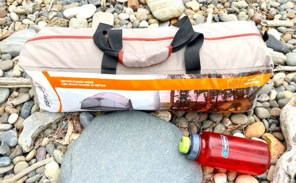This photo shows the Bass Pro Shops Eclipse Refuge Screen House packed up in its included carry bag, alongside a water bottle for size reference.