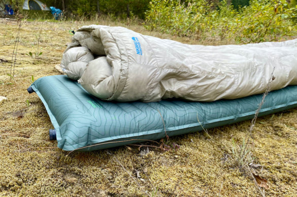 This review photo shows the Therm-a-Rest NeoAir Topo Luxe Sleeping Pad outside with a sleeping bag near a camping tent.