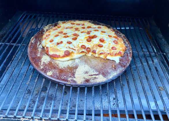 This photo shows a homemade pepperoni pizza cooking on a pizza stone on a pellet grill.