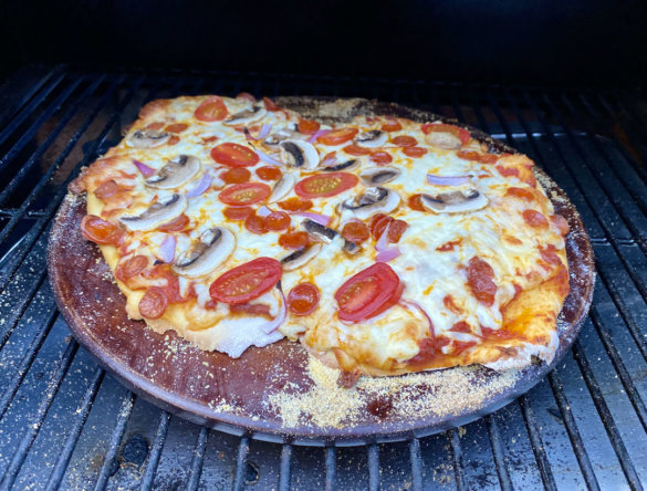 This photo shows a pizza being cooked on a pizza stone inside of a pellet grill.