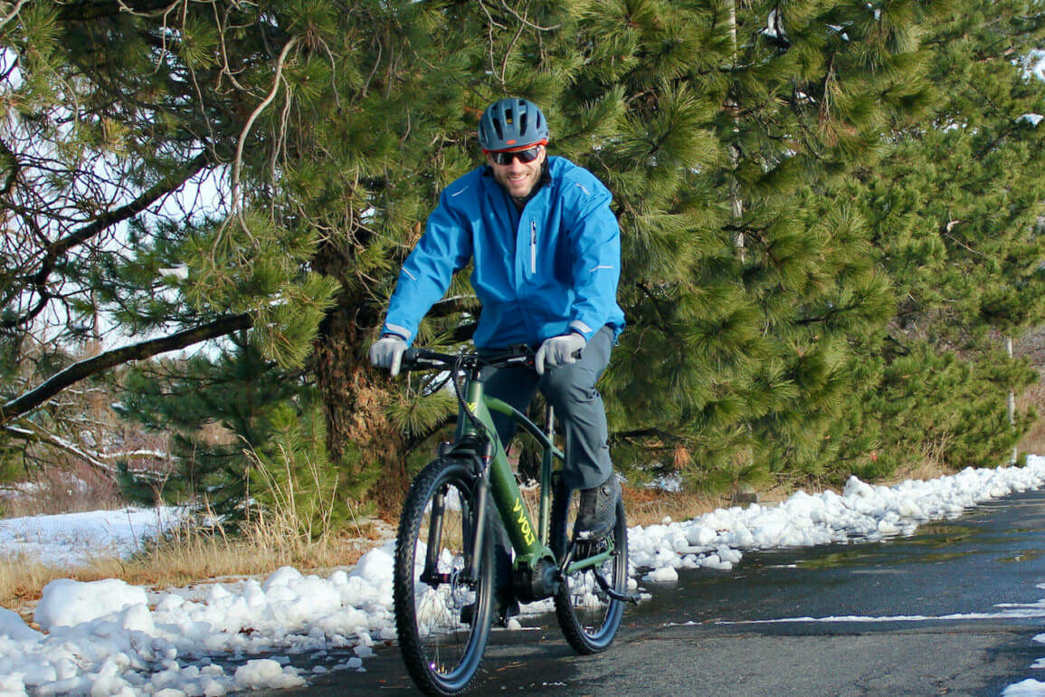 This photo shows the author riding a Vvolt Sirius ebike while wearing the Showers Pass Transit Jacket CC during the testing and review process.