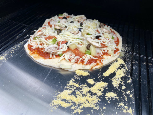 This photo shows the author sliding an uncooked pizza onto a Traeger pellet grill with the Weber Pizza Paddle.