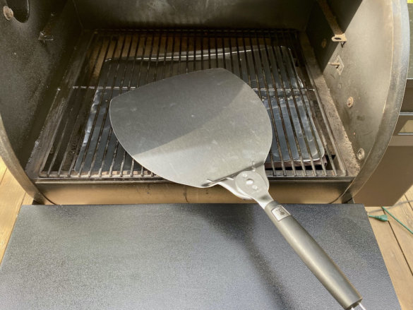 This photo shows the Weber Pizza Paddle near a pellet grill. 