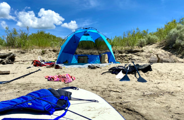 This photo shows the L.L.Bean Sunbuster pop-up sunshade set up on a beach with an inflatable standup paddle board in the foreground.
