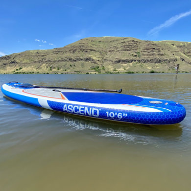 This photo shows the Bass Pro Shops Ascend Inflatable Stand-Up Paddleboard floating on a lake.