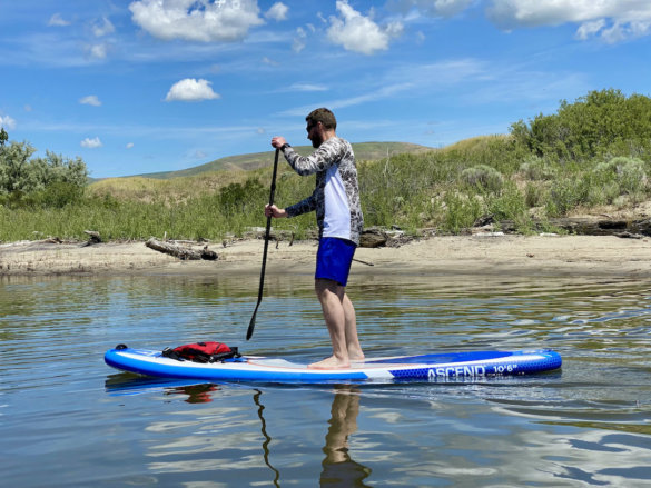 This photo shows the author paddling the Bass Pro Shops Ascend Inflatable Stand-Up Paddleboard Package on a lake.