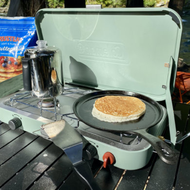 This photo shows the Coleman Cascade 222 two-Burner Camping Stove with a coffee pot and pancake during the testing and review process.