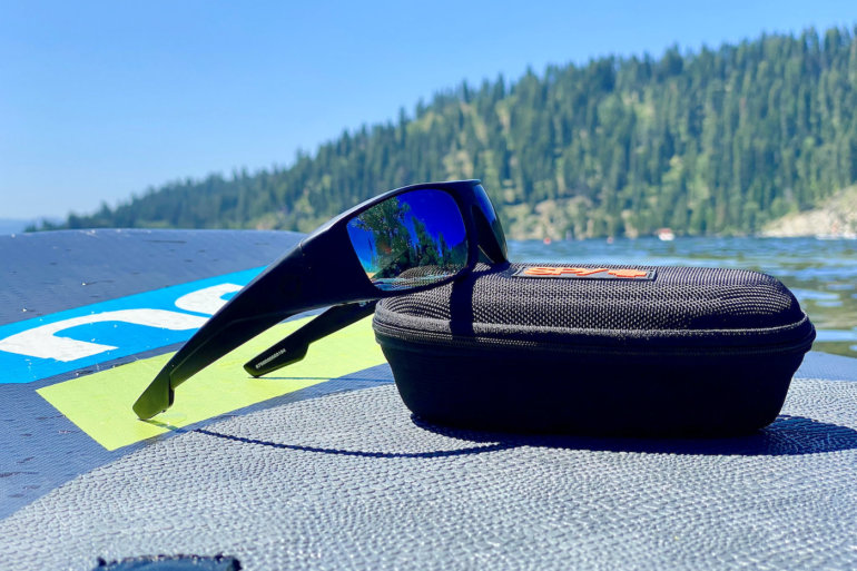 This photo shows the SPY+ Logan sunglasses with Happy Boost lens technology outside on an iSUP paddleboard on a lake.