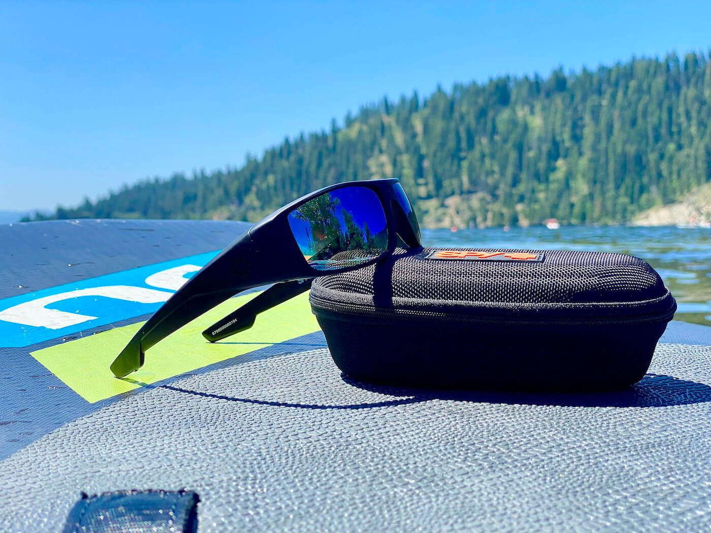 This photo shows the SPY+ Logan sunglasses with Happy Boost lens technology outside on an iSUP paddleboard on a lake.