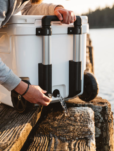 This photo shows the handle and wheels and drain plug on the YETI Roadie 48 cooler behind used on a dock.