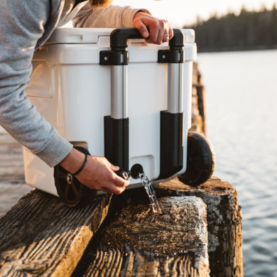 This photo shows the handle and wheels and drain plug on the YETI Roadie 48 cooler behind used on a dock.