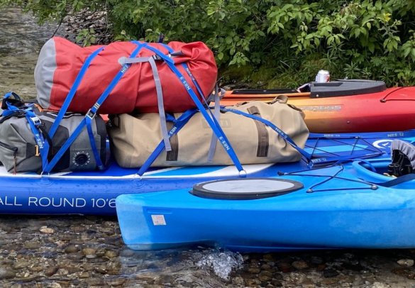 This photos shows the YETI Panga 100L Waterproof Duffel strapped to a standup paddleboard near some kayaks.