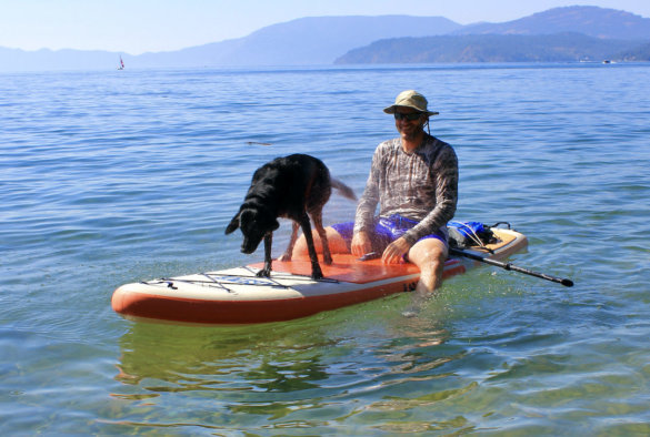 This photo shows the author and a dog sitting on the ISLE Pioneer 2.0 Inflatable Paddle Board in lake.