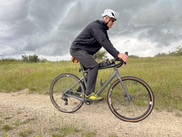 This photo shows the author riding a gravel bike while testing the Showers Pass Timberline Rain Pants.