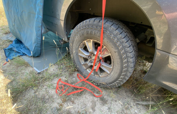 Kelty Backroads Shelter attaches to the wheels of a vehicle with a red strap.