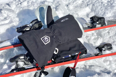This photo shows the Hestra Army Leather Heli Ski Mitts outside on a pair of downhill skis on snow during the testing and review process.